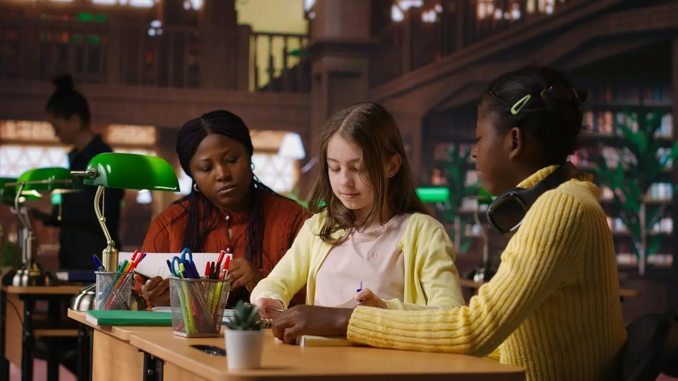 Девочки-предподростки и их преподаватель вместе работают над школьными заданиями в библиотеке.